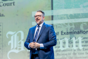 AANA CEO Bill Bruce addresses attendees at the 2026 AANA Annual Congress in front of a display about nurse anesthesiology history.