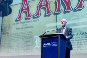 Tracy Young speaking at the 2026 AANA Annual Congress podium with a historical AANA document projected behind him.