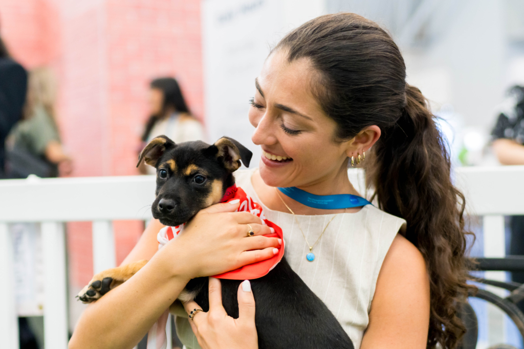 Smiling attendee holds a black and tan puppy wearing a red bandana at the 2026 AANA Annual Congress in Boston.