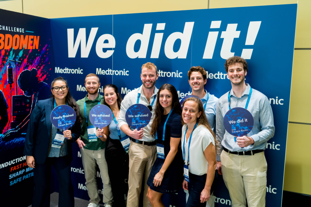 AANA Annual Congress 2026 Escape Room participants hold completion signs in front of a Medtronic escape room backdrop.